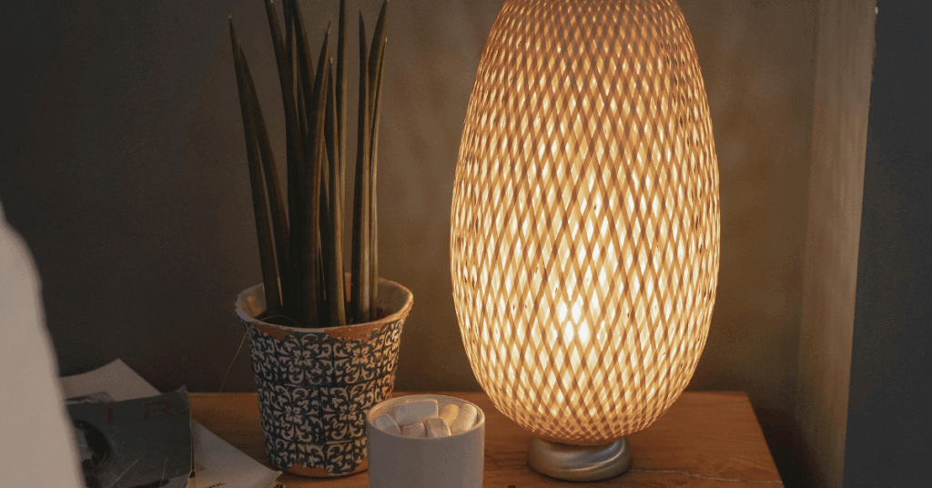 a table lamp with wooden slats that give a lovely effect the wall, sat next to a plant and a pot