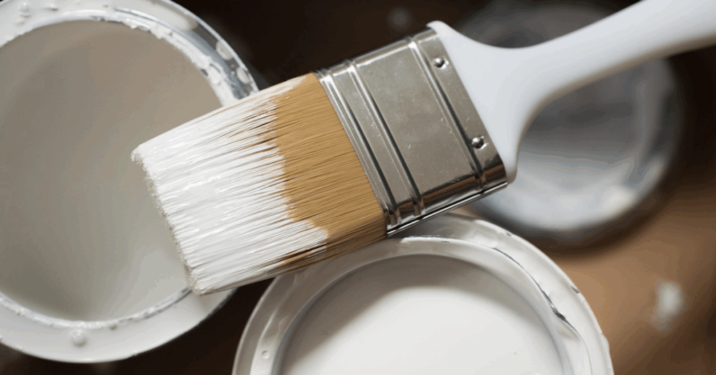 3 white tins of paint with a paintbrush laid across the top